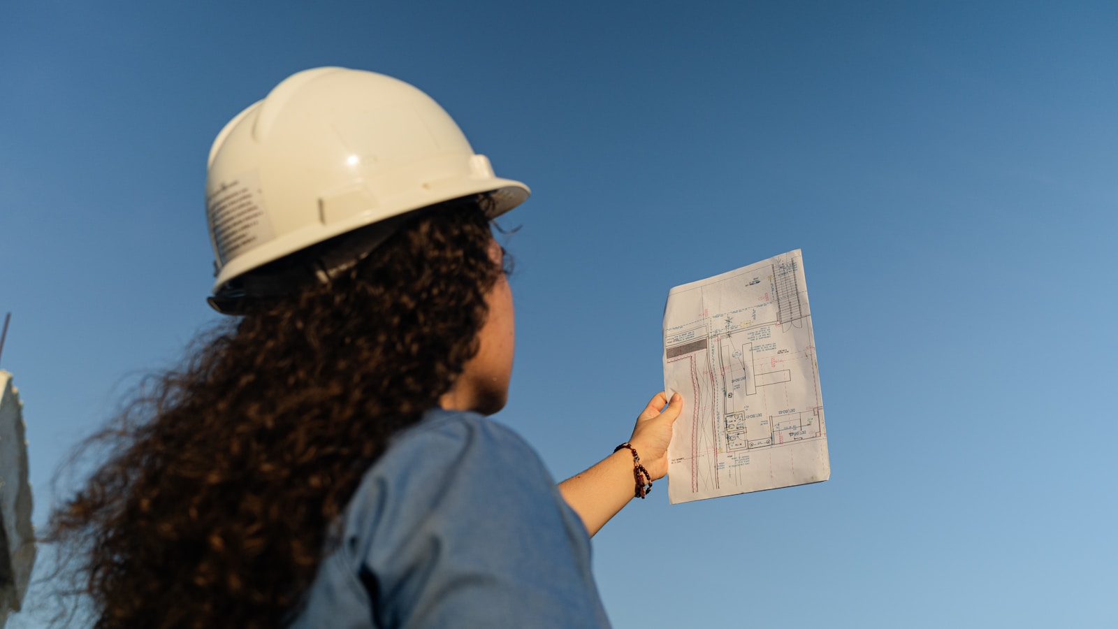 Técnica de capacete branco segurando uma planta de obra contra o céu